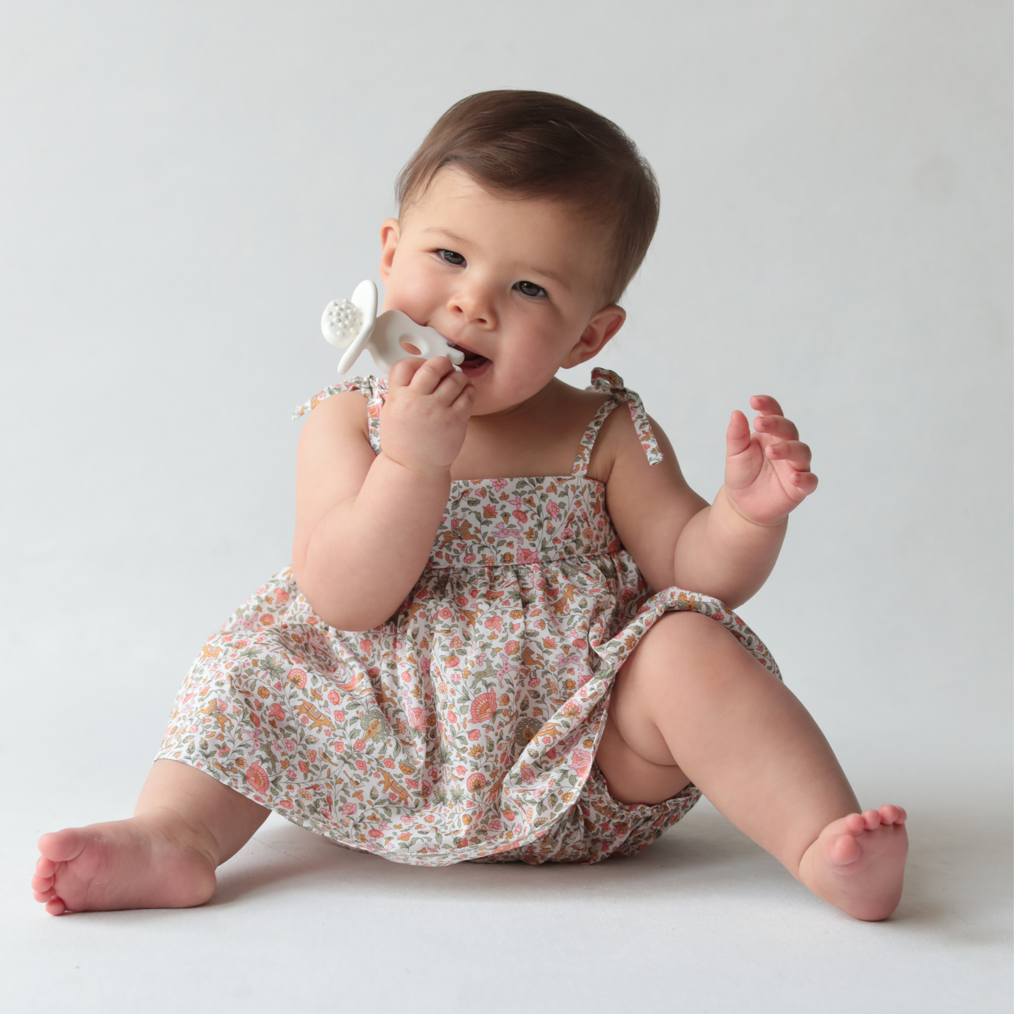 Baby in a floral dress sitting on a plain background