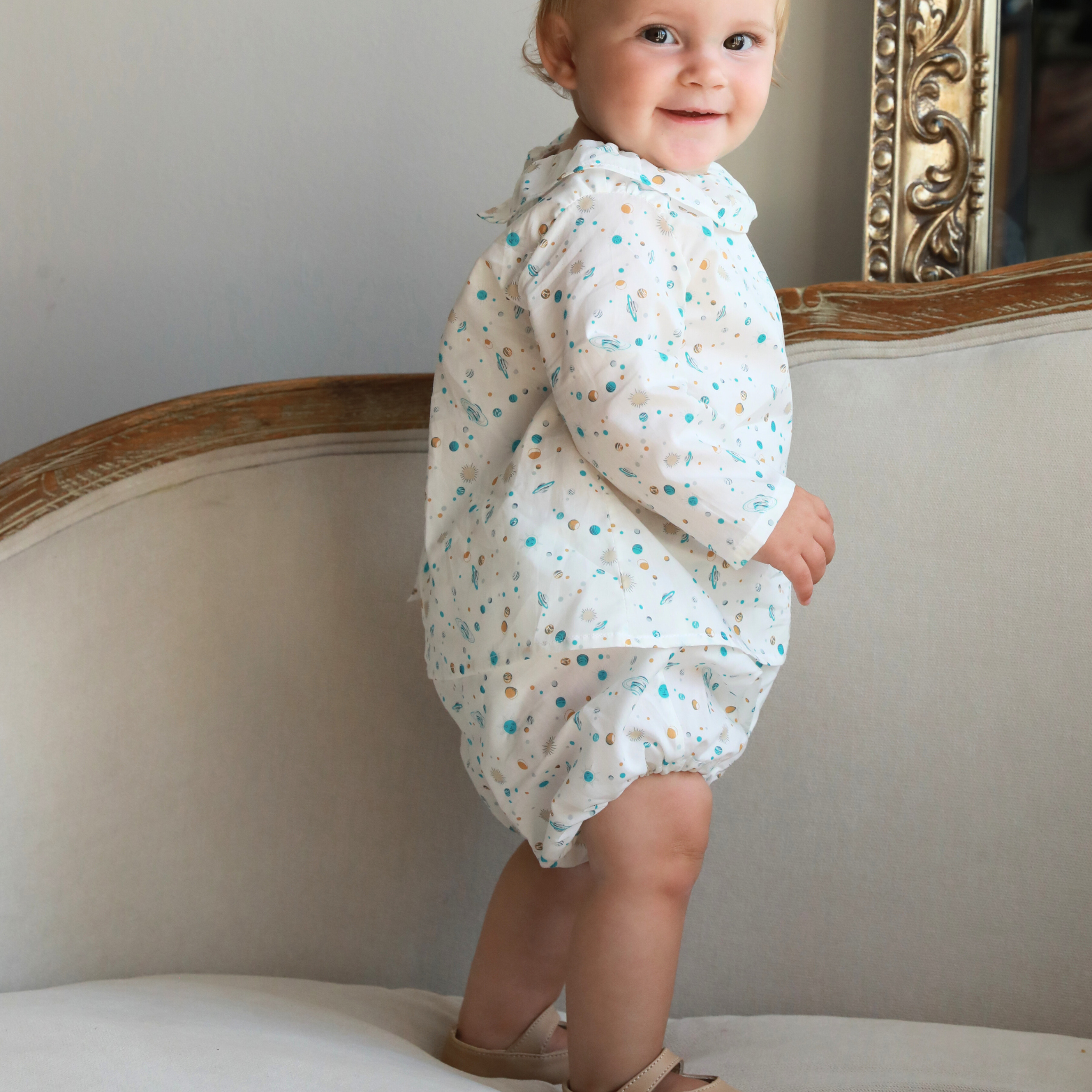 Baby in a floral romper standing on a couch