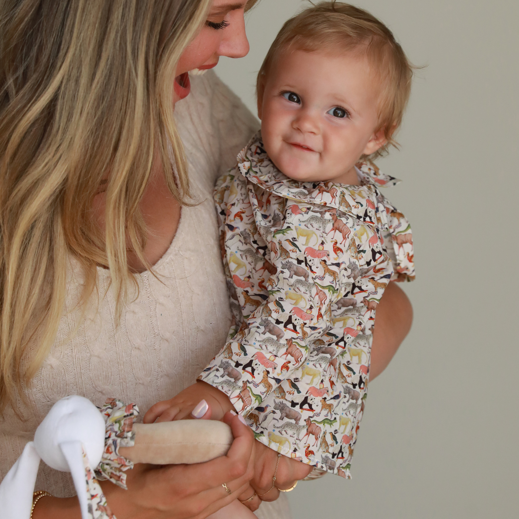 Woman holding a baby wearing a patterned outfit against a neutral background